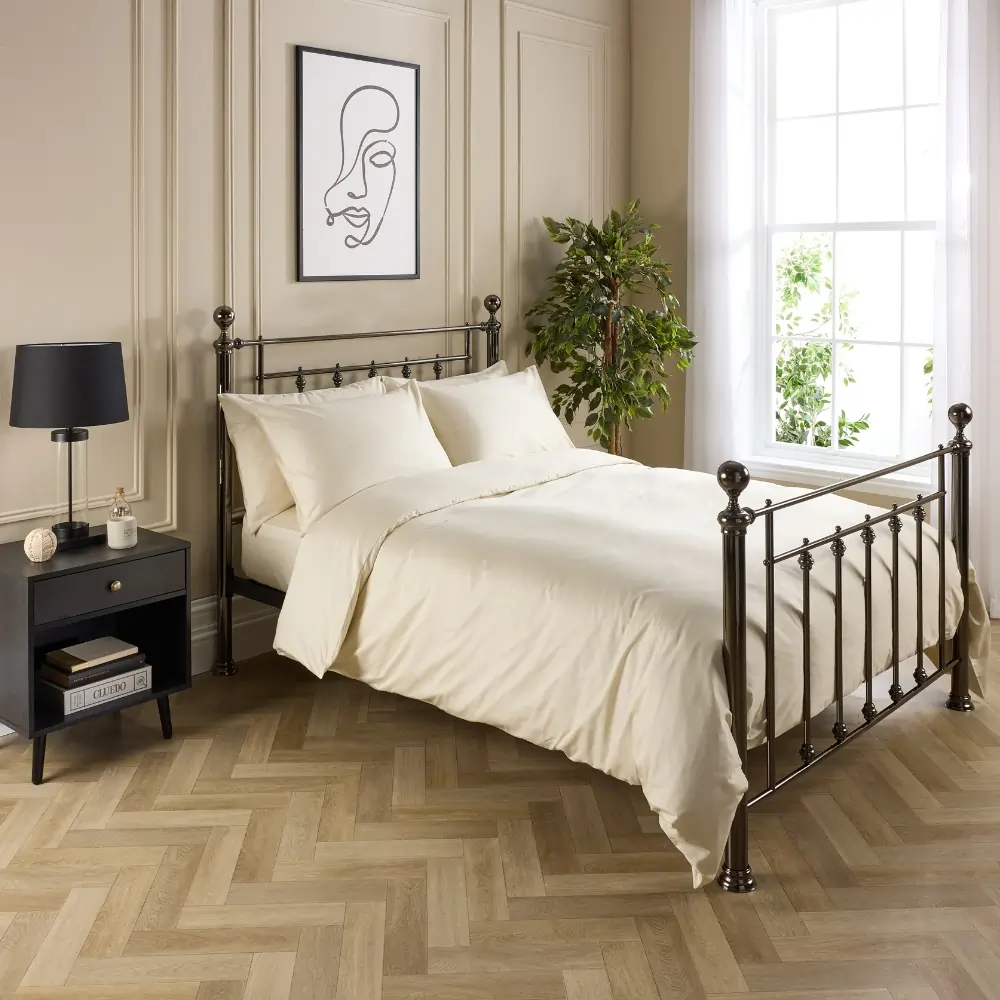 A hotel quality cream coloured cotton duvet cover and pillowcases covering a duvet and pillows on a metal framed bed in a contemporary bedroom.