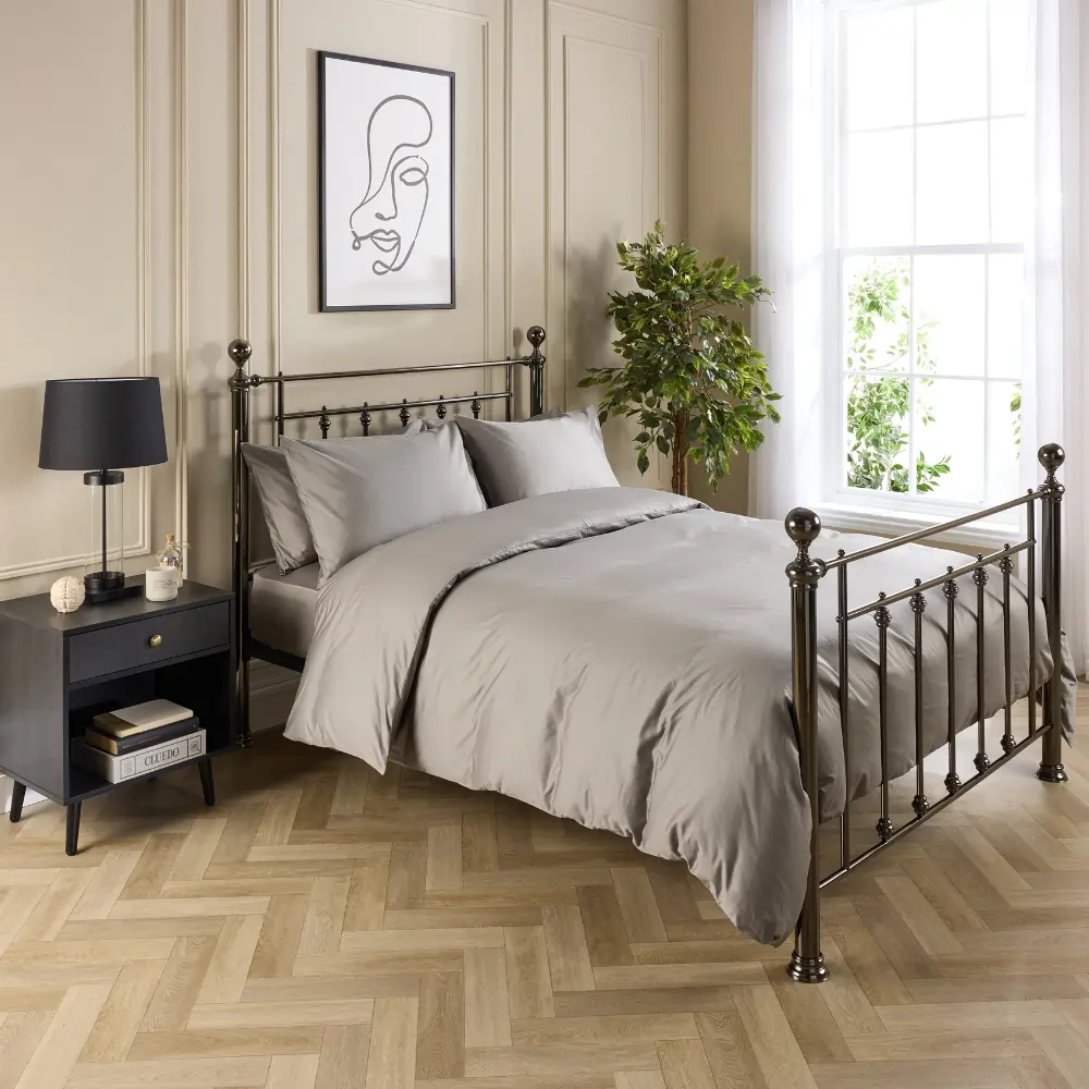 A hotel quality grey coloured cotton duvet cover and pillowcases covering a duvet and pillows on a metal framed bed in a contemporary bedroom.