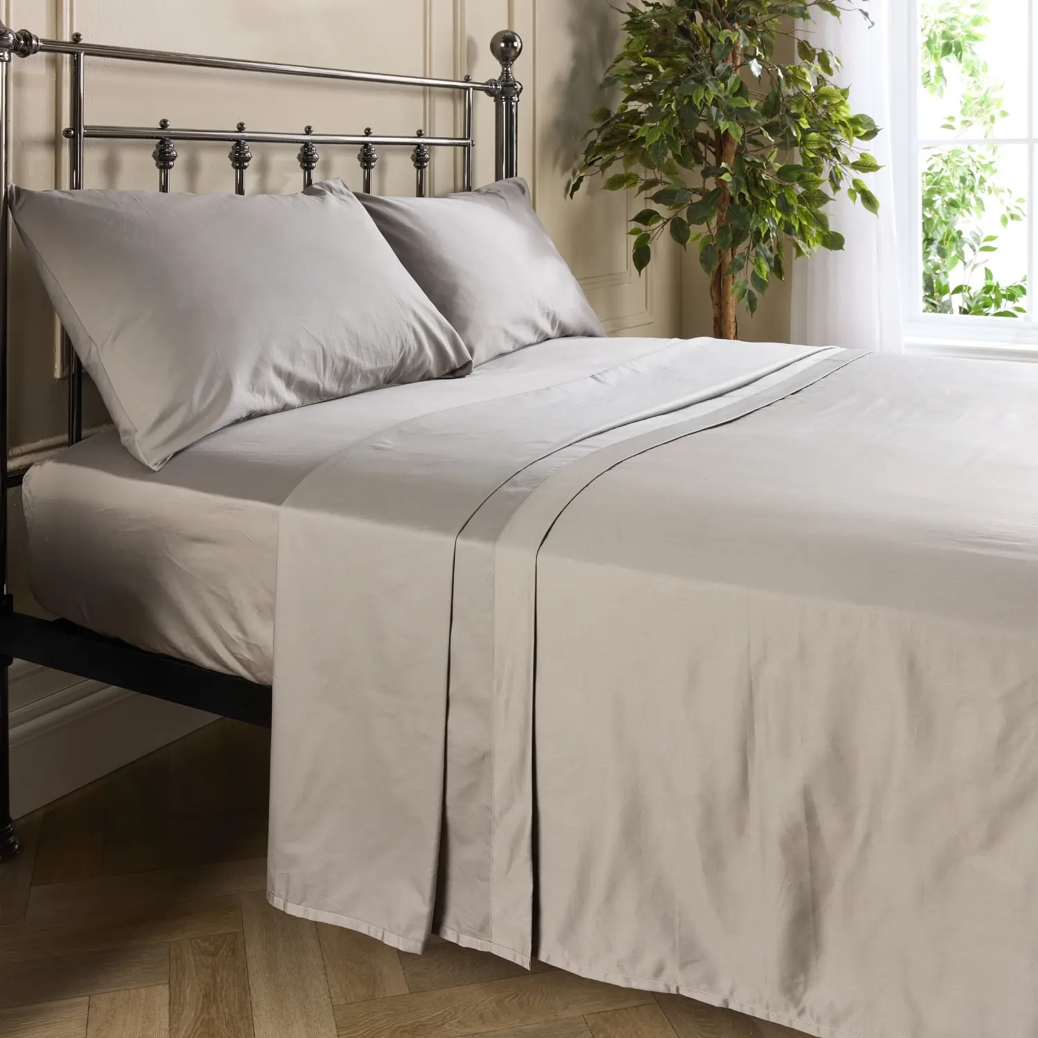 A side view of a hotel quality grey coloured cotton flat bed sheet on a metal framed bed in a contemporary bedroom.