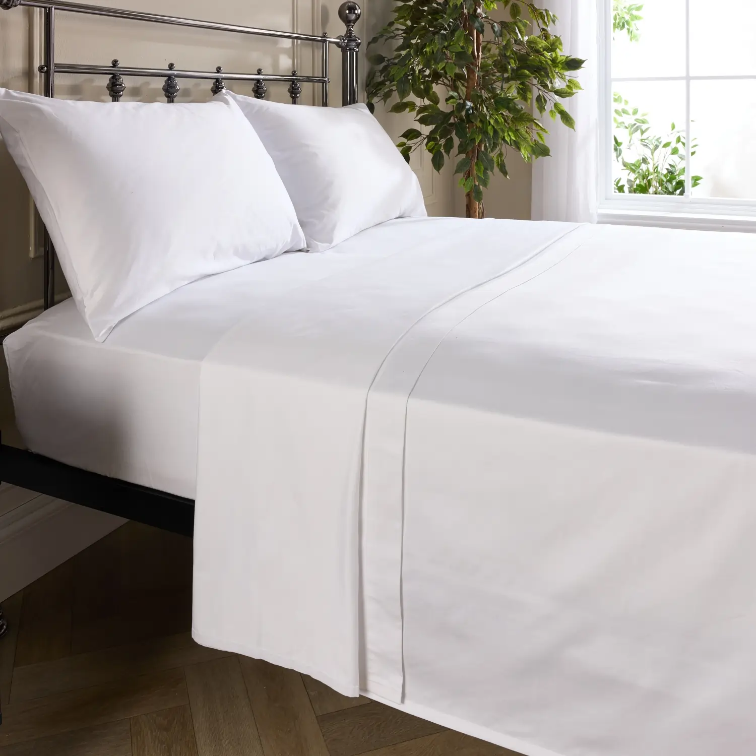 A side view of a hotel quality white cotton flat bed sheet on a metal framed bed in a contemporary bedroom.