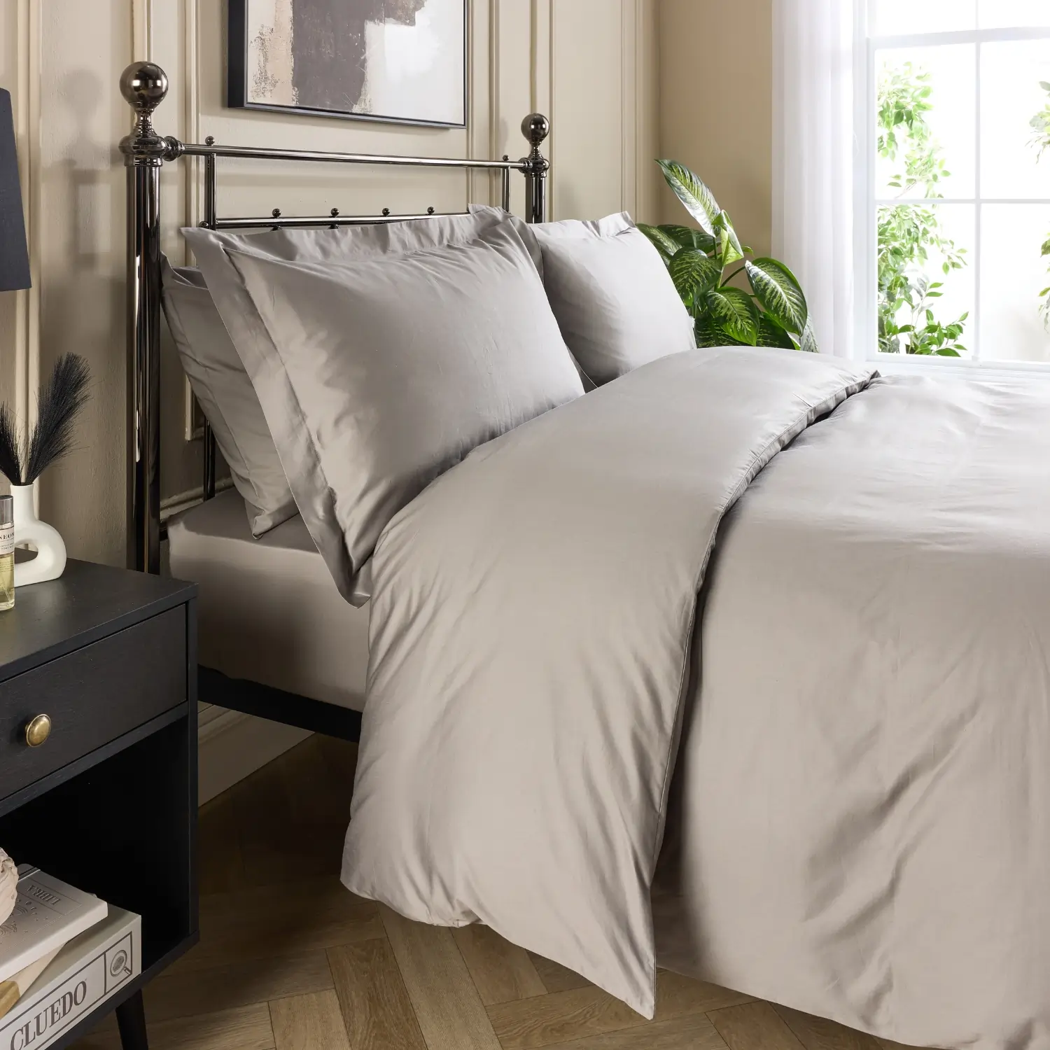 A side view of a hotel quality grey coloured cotton 480 thread count duvet cover and pillowcases covering a duvet and pillows on a metal framed bed in a contemporary bedroom.