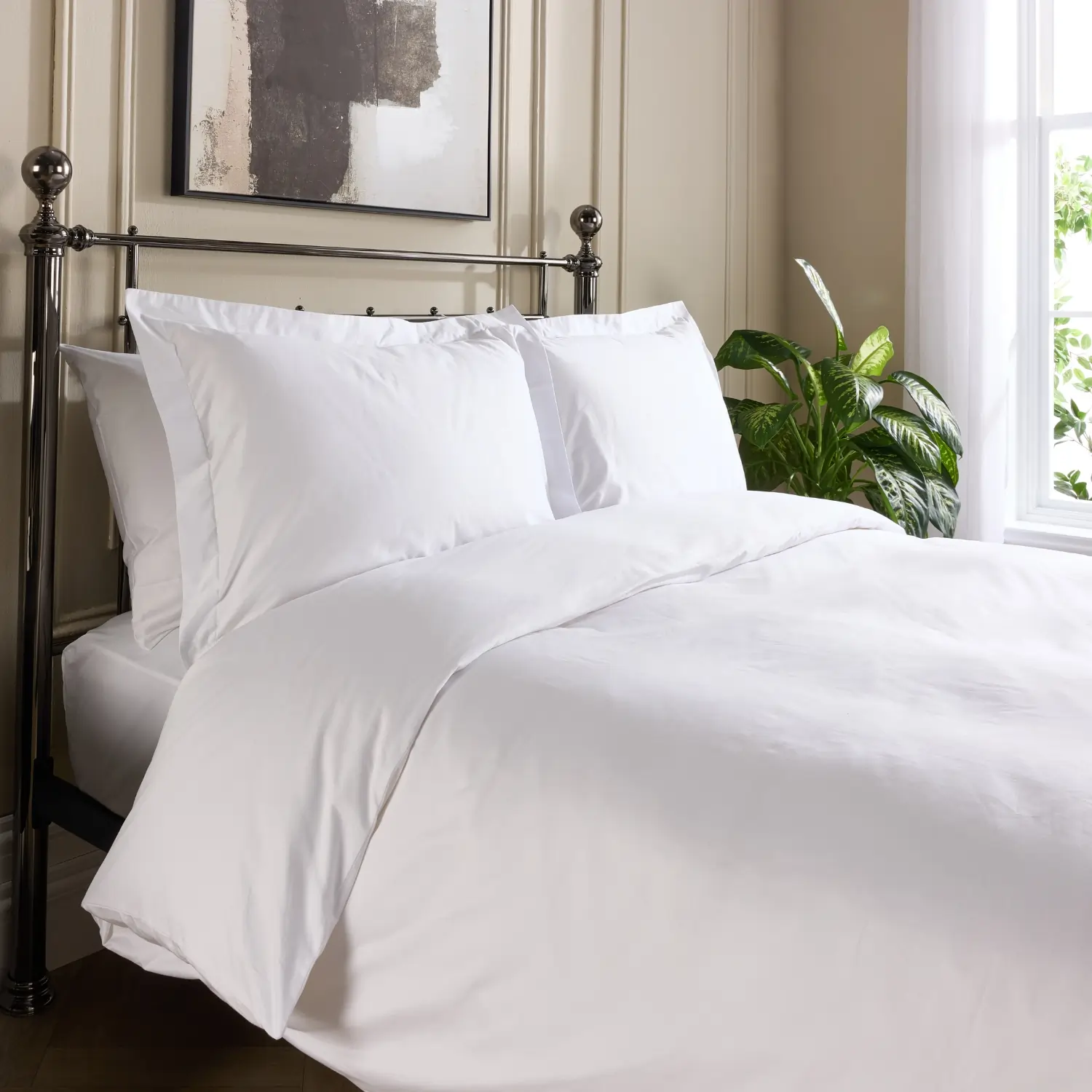 A side view of a hotel quality white cotton 480 thread count duvet cover and pillowcases covering a duvet and pillows on a metal framed bed in a contemporary bedroom.