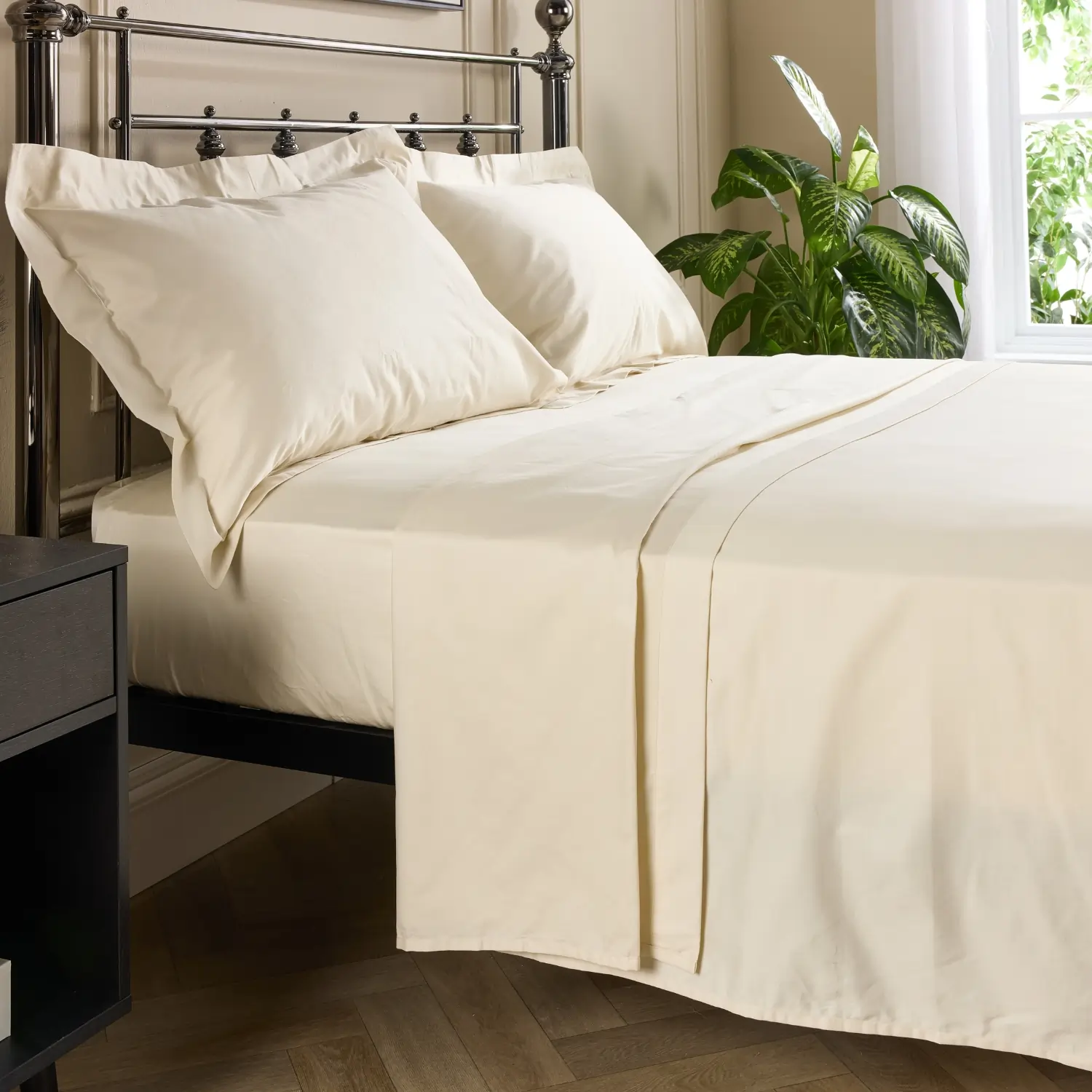 A side view of a hotel quality cream coloured 480 thread count cotton flat bed sheet on a metal framed bed in a contemporary bedroom.