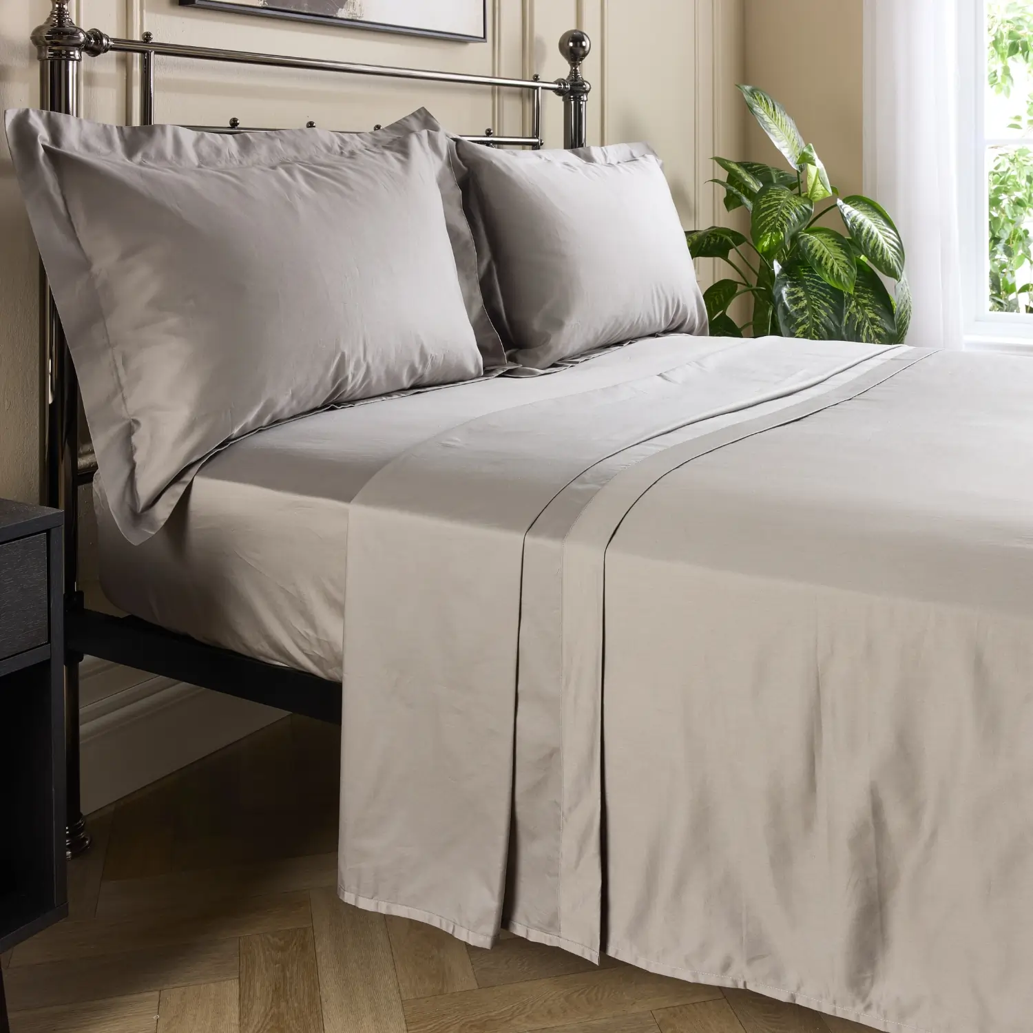 A side view of a hotel quality grey coloured 480 thread count cotton flat bed sheet on a metal framed bed in a contemporary bedroom.