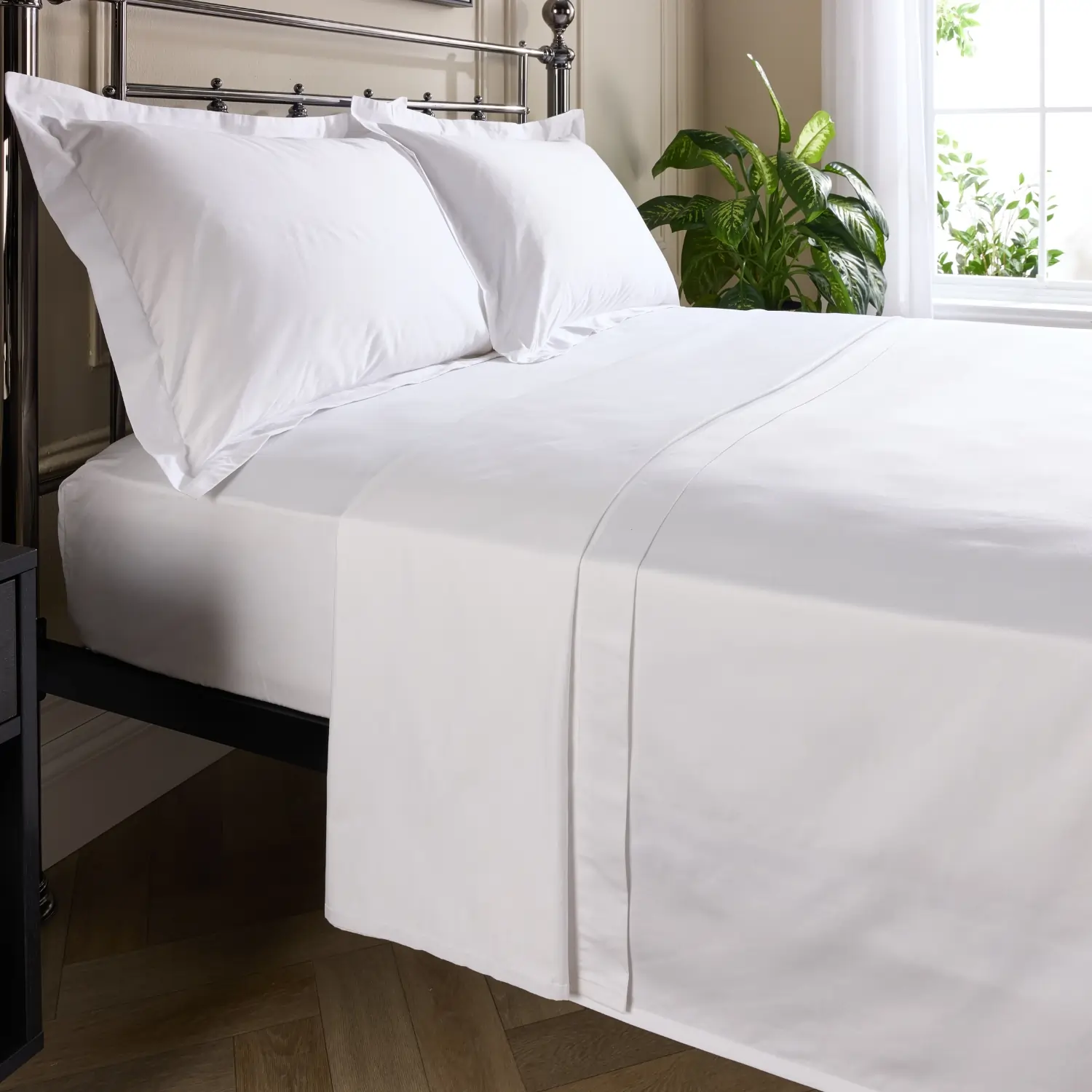 A side view of a hotel quality white 480 thread count cotton flat bed sheet on a metal framed bed in a contemporary bedroom.