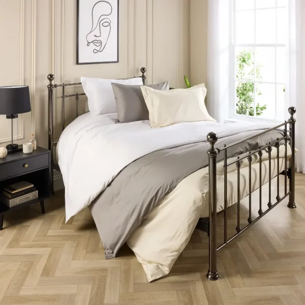 Three hotel quality cotton duvet covers on a bed inside a contemporary bedroom. There is a cream, white, and grey duvet cover covering three duvets. The bed is made of a metal frame.