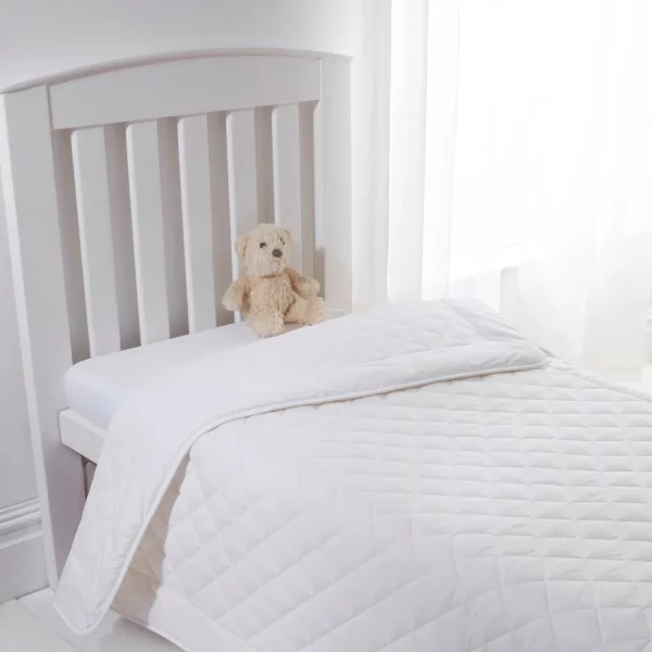 A Clair De Lune anti-allergy 4 tog wool cot bed duvet on a child's bed. There is also a brown teddy bear sitting on the mattress.