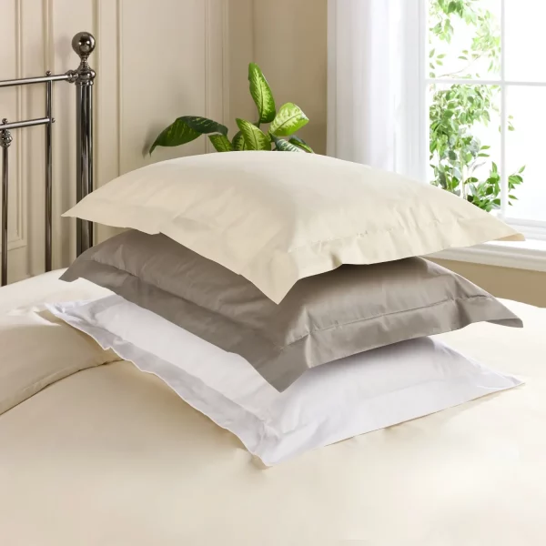 Three Hotel Pure Luxury Oxford pillowcases encasing pillows stacked on top of each other. In crea, grey and white.