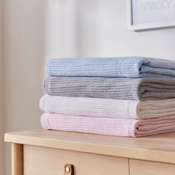 Stack of cellular blankets for use with babies. There is a blue, grey, white, and pink blanket stacked on top of each other.