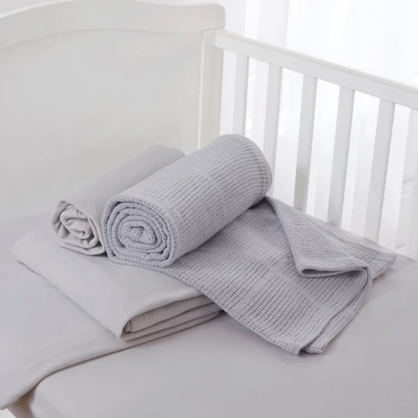 A grey cot bed starter set from Clair De Lune sitting in a cot. It contains a fitted sheet, cellular blanket, and polar fleece blanket.