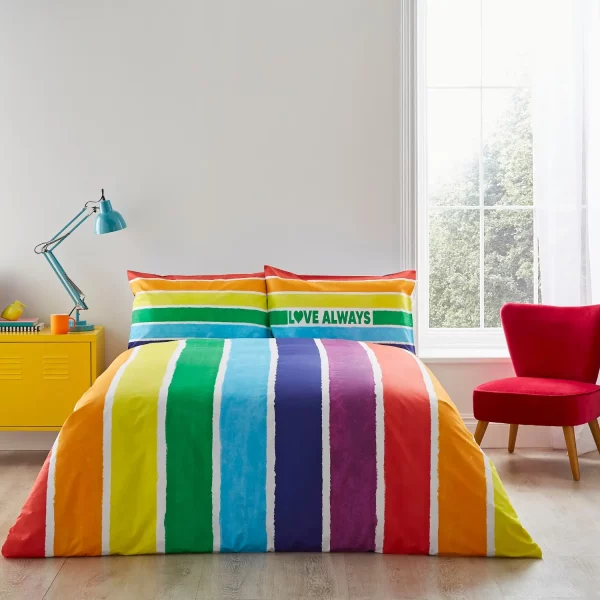 A multi-coloured rainbow Pride themed duvet cover and pillowcase set from Martex Pride covering a bed in a modern bedroom. It says 'Love Always' on one of the pillowcases.