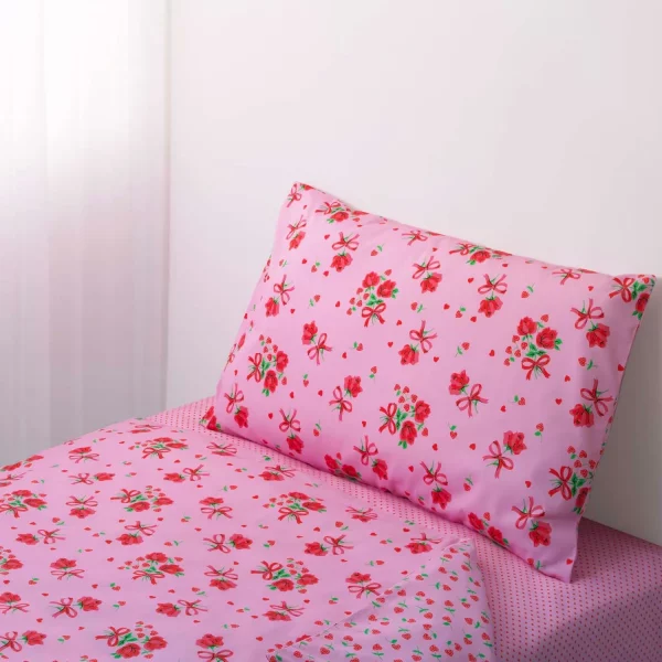 A pink strawberry rose duvet cover and pillowcase set from Rachel Riley. The pattern includes roses with a red bow tied underneath them, and small red love hearts.