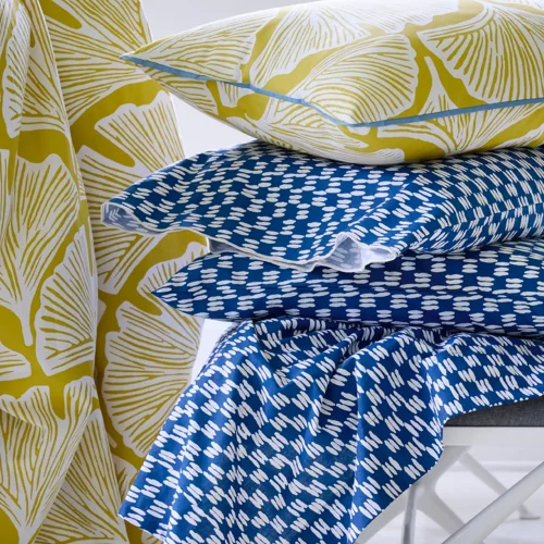 A close up of a golden mustard feather palm patterned duvet cover and pillowcase. Also pictures is a painted blue check fitted sheet, which is available separately.