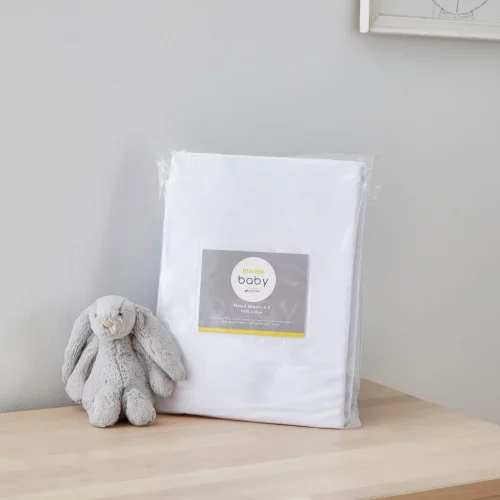 A white moses basket fitted sheet from Martex Baby in its packaging. There is a grey toy bunny next to it.