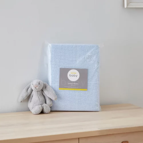 A blue cellular blanket from Martex Baby in its packaging. There is a grey toy bunny sitting next to it.