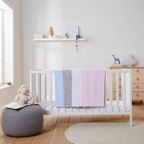 Blue, grey, white, and pink cellular blankets hanging off a cot in a children's bedroom