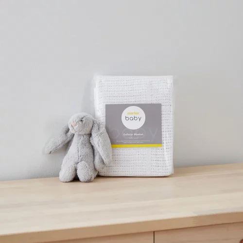 A white cellular blanket from Martex Baby in its packaging. There is a grey toy bunny sitting next to it.