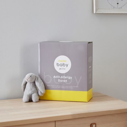 Grey and yellow packaging for a Martex Baby anti-allergy 4 tog duvet for use in a cot bed. The packaging is sitting on a chest of drawers and there is a small grey toy bunny sitting next to it.