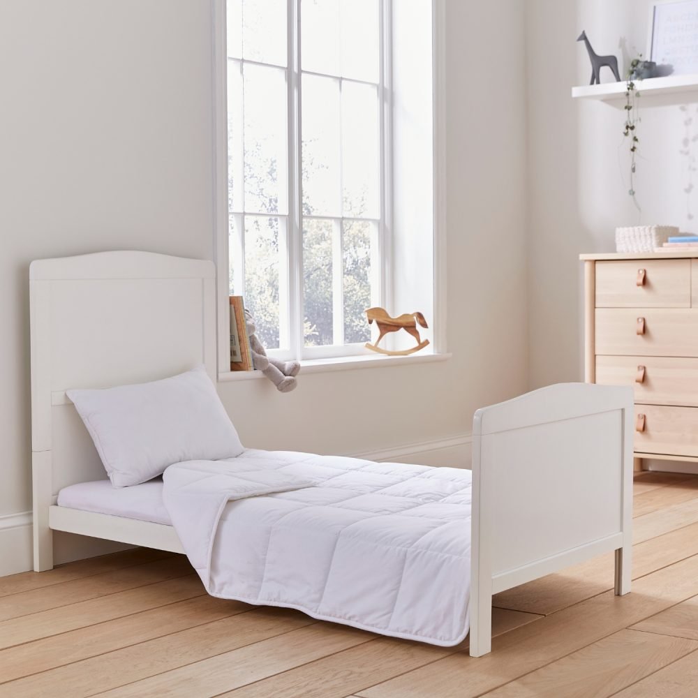 A Martex Baby anti-allergy 4 tog cot bed duvet sitting on a bed in a child's bedroom. The duvet is slightly folded back. There is also a pillow sitting against the headboard.