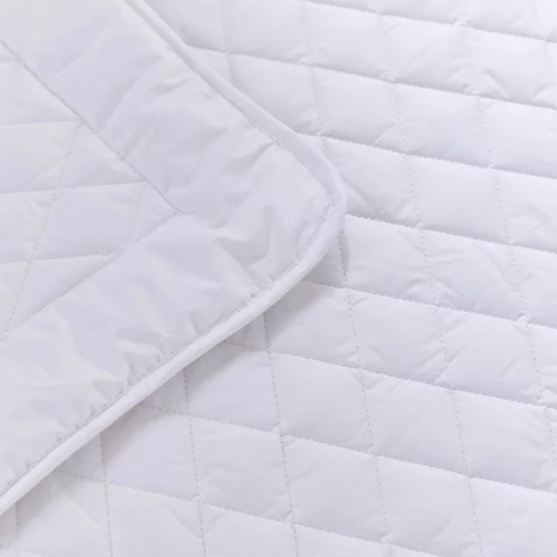 A close up look at a white 4 tog cot bed wool duvet from Martex Baby. The duvet has a diamond grid design. The duvet is slightly folded back.