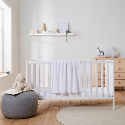 A white cellular blanket hanging off the edge of a a cot in a child's bedroom. The blanket is part of the Martex Baby cot bed starter set, the rest of which is not pictured.