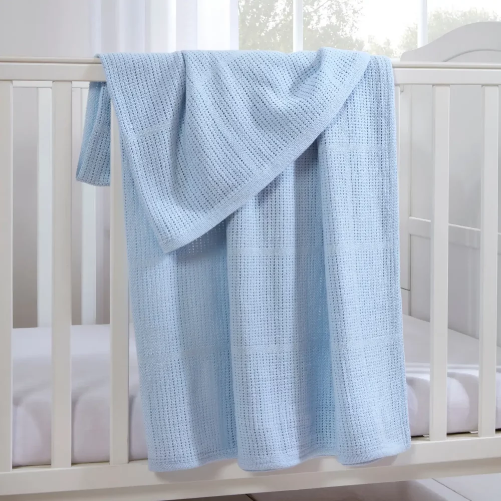 A blue Clair De Lune cotton cellular blanket hanging from a cot