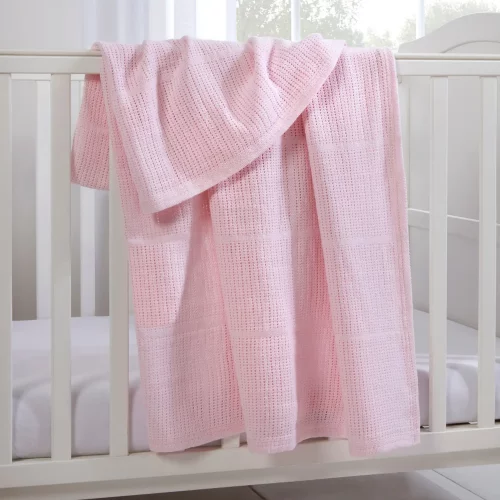 A pink Clair De Lune cotton cellular blanket hanging from a cot