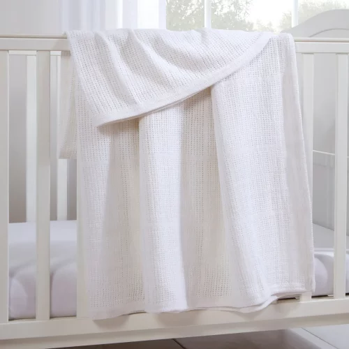 A white Clair De Lune cotton cellular blanket hanging from a cot