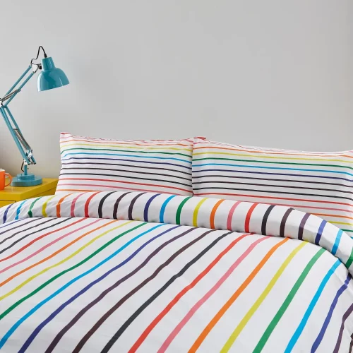 A multi-coloured rainbow striped Pride themed duvet cover and pillowcase set from Martex Pride covering a bed in a modern bedroom.